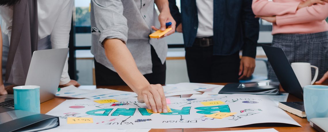 Happy young Asian businessmen and businesswomen meeting brainstorming ideas about new paperwork project colleagues working together planning success strategy enjoy teamwork in small modern office.