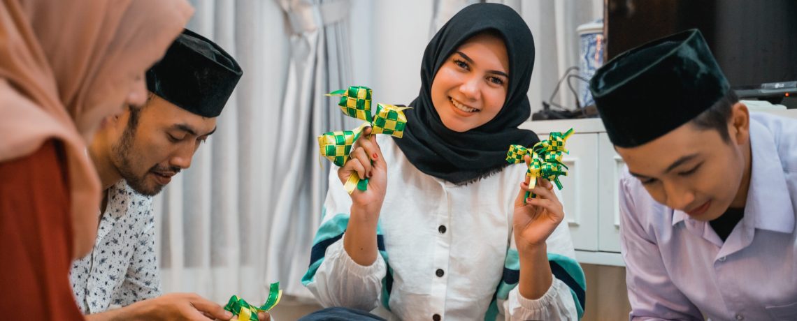 smiling veiled woman holding woven ketupat ornaments for Eid decoration