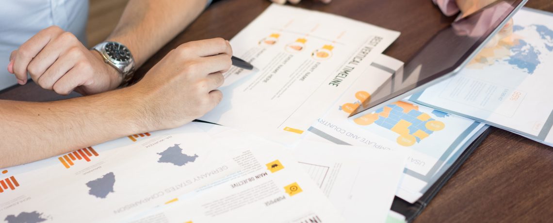 Hands of businesspeople discussing marketing reports and presentation on tablet. Close-up of young Caucasian businessman and businesswoman sitting at table and working over documents. Teamwork concept